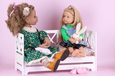 two dolls are sitting on a bench and one doll is holding a stuffed animal in her lap