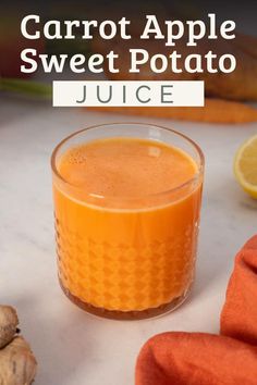 carrot apple sweet potato juice in a glass on a white table with oranges and ginger