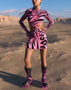 a woman is standing in the desert wearing pink and black clothing with zebra print on it