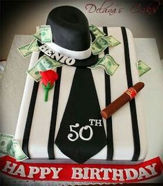 a 50th birthday cake with money and a hat on the top, sitting in front of a red ribbon