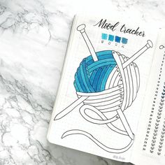 an open notebook with crochet needles and balls of yarn in it on a marble surface