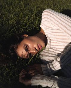 a woman laying in the grass with her eyes closed and looking at the camera,