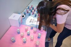 a woman looking at candles on a table with pink and blue cloth covering the table