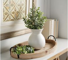 a white vase sitting on top of a wooden tray next to a potted plant