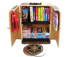 an old fashioned wooden bookcase with various books and snacks on it, sitting next to a movie projector