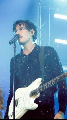 a man holding a white guitar while standing in front of a microphone on top of a stage