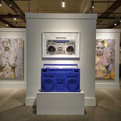 a blue boombox sitting on top of a white pedestal in front of two paintings