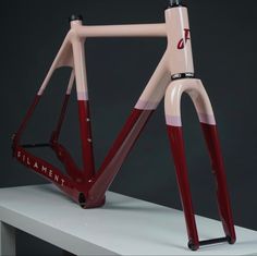 a pink and red bike frame sitting on top of a white table next to a black wall