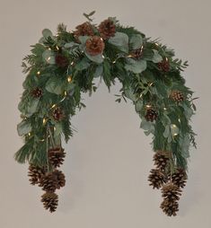 a christmas wreath with pine cones and greenery hanging from the front, on a wall