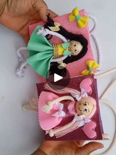 a hand holding two small dolls on top of a pink bag