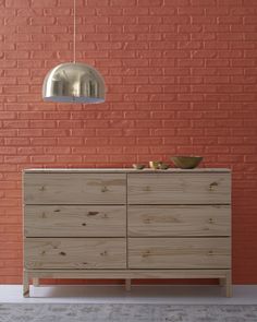 a wooden dresser sitting in front of a brick wall with a light hanging over it