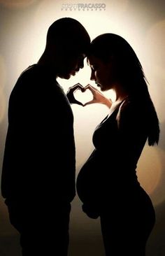 a pregnant couple standing next to each other with their hands in the shape of a heart