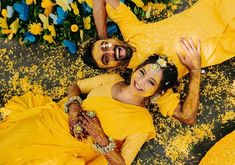 two people dressed in yellow are laying on the ground with flowers all over their bodies