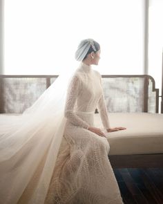 a woman sitting on top of a bed wearing a white dress and veil over her head