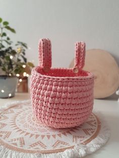 a pink crocheted basket sitting on top of a white doily next to a potted plant