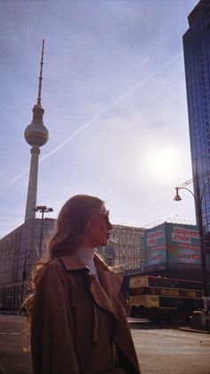 a woman standing on the side of a road next to a tall building with a tv tower in the background