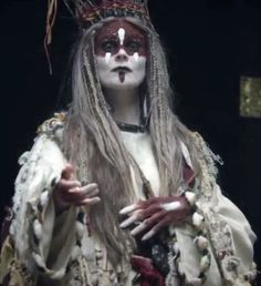 a woman with white makeup and long hair wearing a costume that has feathers on it's head