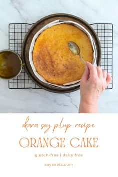 an orange cake on a cooling rack with a hand holding a spoon over the top