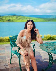 a beautiful woman sitting on top of a green chair next to a table with a lake in the background