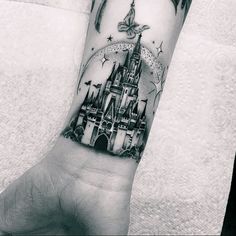 a black and white photo of a castle tattoo on the left hand with a butterfly flying over it