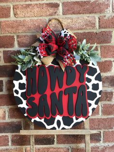 a red and black door hanger with the words howdy santa on it hanging from a brick wall