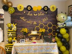 a table with balloons and decorations for a bee themed birthday party on the wall behind it is a sign that says he she said will be happy