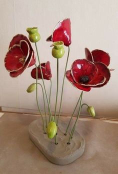 some red flowers are in a vase on a table with a white wall behind them