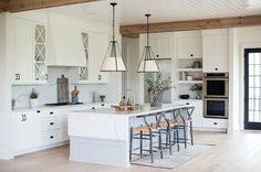 a large kitchen with white cabinets and wooden floors is pictured in this image, there are four stools at the center of the island