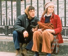 a man and woman sitting on a bench next to each other in front of a fence