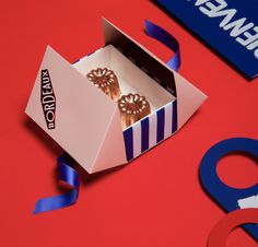 an open box with two donuts in it on a red surface next to blue and white ribbons