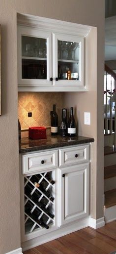 a wine rack in the corner of a kitchen with white cabinets and black counter tops