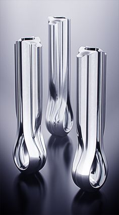 three shiny silver vases sitting on top of a table next to each other in front of a gray background