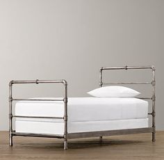 a metal bed frame with white sheets and pillows on top of wooden floor next to gray wall