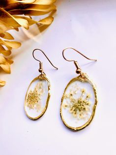 the dandelion earrings are hanging from gold earwires on a white surface