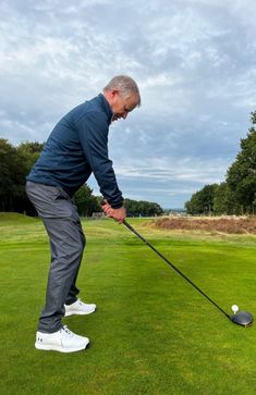 an older man hitting a golf ball on the green with his club in front of him