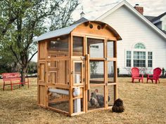 a chicken coop with two chickens in it on the grass next to a red lawn chair