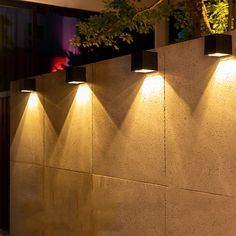 three lights on the side of a wall next to a planter and potted tree