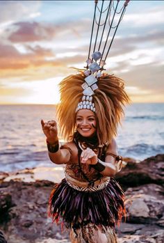 a woman in a costume standing on rocks near the ocean with her hands up and arms out