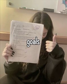 a woman holding up a piece of paper with the words goals written in front of her