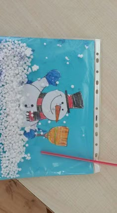 a snowman is holding a pencil in front of a drawing on a piece of paper