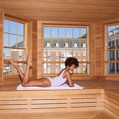 a woman laying on top of a wooden sauna in front of two large windows