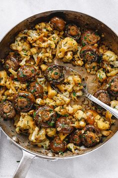 a skillet filled with mushrooms and cauliflower on top of a white table