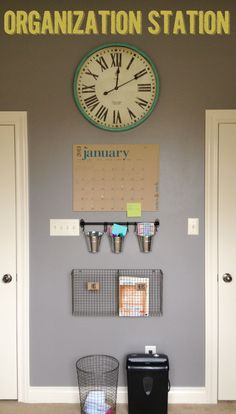 a large clock mounted to the side of a wall next to a trash can and bin