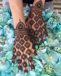 a woman's hands with henna tattoos on them and flowers in the background