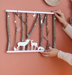 a person holding up a paper cut out of trees with deer and birds on it