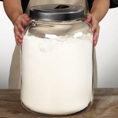 a person holding a large jar filled with white flour on top of a wooden table