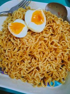 an image of noodles and eggs on a plate with fork, spoon and utensils