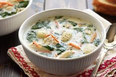 two white bowls filled with soup on top of a wooden table next to silverware