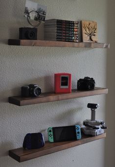 two wooden shelves with video game controllers and cameras on them, along with bookshelves