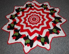 a red and white crocheted christmas star with holly decorations on the center is shown